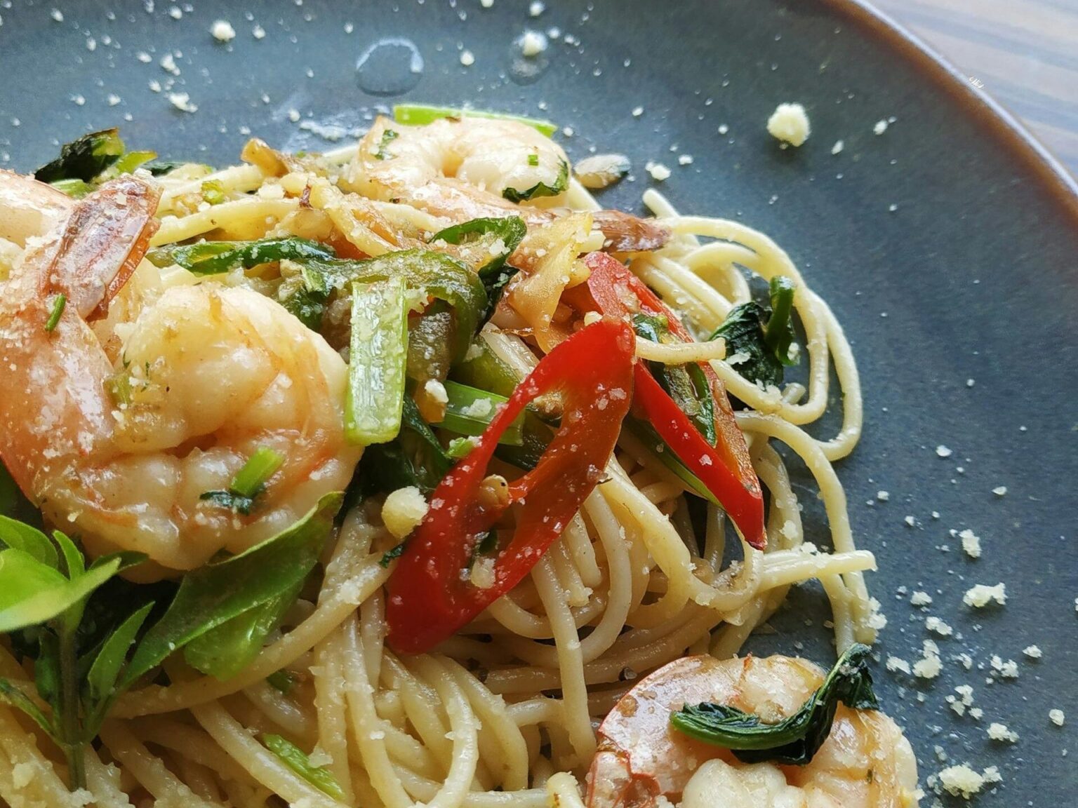 Appetizing shrimp pasta garnished with fresh chili and herbs in a close-up view.